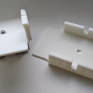 May include: Two white plastic 3D printed camera mounts. One mount has a screw hole in the center and the other has a small hole in the center.