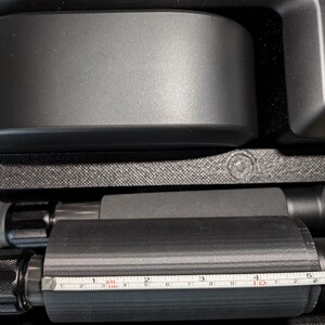 May include: A close-up of a black tripod with a ruler measuring 10 inches. The tripod is made of metal and has a black rubber grip.
