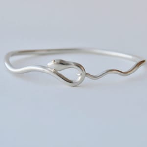 以下が含まれることがあります： 蛇の形をした銀製のバングルブレスレット。蛇の頭には金のアクセントが施されています。