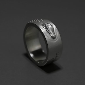 May include: A silver ring with an alligator head design and the inscription "Undercover" on the side.