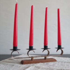 May include: A metal candle holder with four arms, each holding a red candle. The holder is made of metal and has a wooden base.