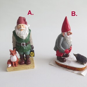 May include: Two small, hand-painted figurines of gnomes with red hats. The gnome on the left is holding a lantern and standing next to a fox. The gnome on the right is standing next to a hedgehog. Both gnomes have white beards and are standing on a base with the WWF logo and the year the figurine was made. The gnome on the left is from 1997 and the gnome on the right is from 2003.
