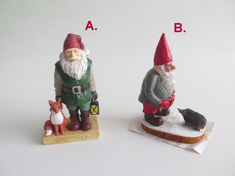 May include: Two small, hand-painted figurines of gnomes with red hats. The gnome on the left is holding a lantern and standing next to a fox. The gnome on the right is standing next to a hedgehog. Both gnomes have white beards and are standing on a base with the WWF logo and the year the figurine was made. The gnome on the left is from 1997 and the gnome on the right is from 2003.