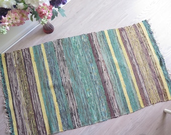 May include: A woven rug with stripes of yellow, green, brown, and gray. The rug has a frayed edge and is made of a natural fiber.