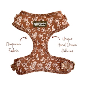 Peut inclure: Un harnais pour chien en néoprène marron avec un motif floral blanc. Le harnais porte le texte "The Love Paws Pet Lover Shop" et est réalisé avec des motifs uniques dessinés à la main.