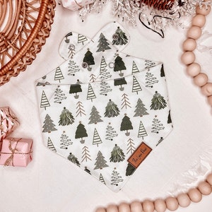 Op de afbeelding: Een witte bandana met een groen-wit kerstboommotief. De bandana heeft een bruin leren label met de tekst "The Love You Give" erop.