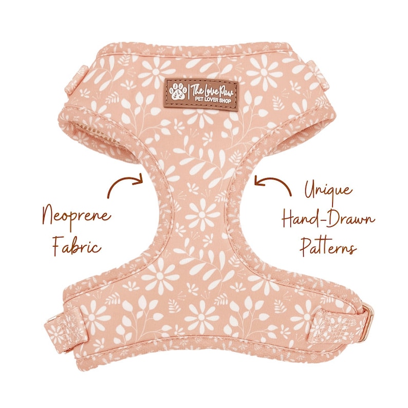 May include: A pink dog harness with a white floral pattern. The harness is made of neoprene fabric and features a unique hand-drawn design. The text "The Love Plus Pet Lover Shop" is printed on the harness.