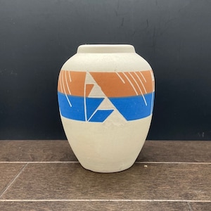 May include: White ceramic vase with a geometric design in shades of orange and blue. The vase has a rounded body and a narrow opening.