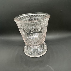May include: A clear glass vase with a decorative floral pattern and a pedestal base.
