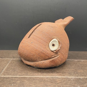 May include: A brown ceramic whale piggy bank with a white glazed eye and a slot on top for coins.