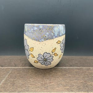 May include: A set of three ceramic mugs with a speckled, matte finish. The mugs are in shades of cream, light gray, and dark gray. Each mug has a simple, minimalist design, perfect for coffee or tea.