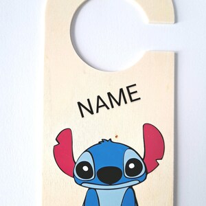 May include: Wooden door hanger featuring a blue Stitch character from Lilo & Stitch. The hanger has a slot at the top for hanging on a door and says "NAME" at the top.