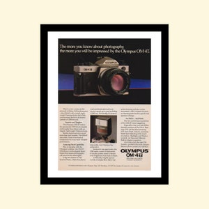 May include: A vintage advertisement for the Olympus OM-4T camera. The ad features a black and silver camera with a lens and a flash unit. The text highlights the camera's features, including its speed, durability, and flash capabilities. The ad also includes the Olympus logo and the tagline "More than just a camera. A masterpiece of perfection."