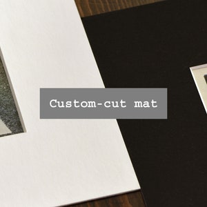 May include: A white mat board with a custom-cut mat opening, next to a black mat board with a picture of a night sky with stars.