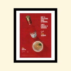 以下が含まれることがあります： 赤と白のストリチナヤ・ウォッカのボトルと、緑のオリーブの入ったマティーニグラスが赤い背景に置かれています。テキストには「Not a creature was stirring. They prefer it shaken. Stoli The Vodka.」とあります。