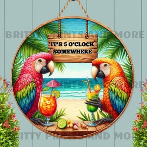 Könnte beinhalten: Rundes Holzschild mit einer Strandszene und zwei Papageien, die Cocktails halten. Auf dem Schild steht "It's 5 O'Clock Somewhere". Die Papageien sind rot, orange, gelb und blau. Der Hintergrund umfasst Palmen, das Meer und einen Sandstrand.