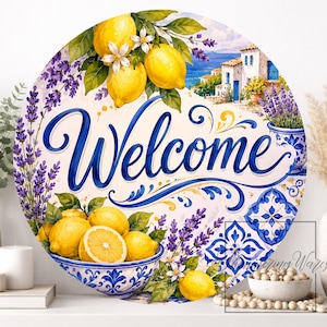 May include: A round decorative sign featuring the word Welcome in blue script. The design includes yellow lemons, purple lavender sprigs, a blue and white patterned bowl, and a coastal Mediterranean building scene with blue accents.