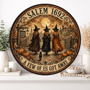 May include: A round wall sign featuring a scene of three witches in pointed hats walking toward a village under a full moon. The text reads SALEM 1692 and A FEW OF US GOT AWAY. The image includes pumpkins, a black cat, and autumn leaves.