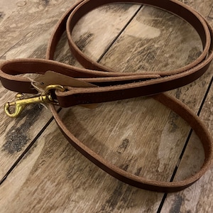 May include: A brown leather dog leash with a brass hook. The leash is folded in half and the hook is visible.