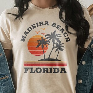 May include: A beige t-shirt with a retro-style graphic design featuring palm trees, a sunset, and the text "Madeira Beach Florida".