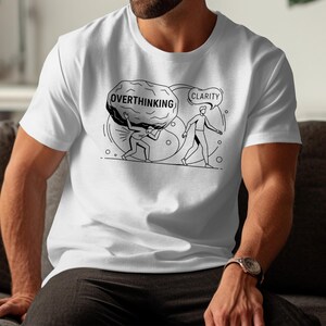 May include: White t-shirt with a black and white graphic illustrating the concept of overthinking versus clarity. The design shows a person carrying a boulder labeled "Overthinking" and another walking towards "Clarity".