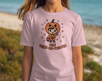 May include: A pale pink t-shirt with a cartoon illustration of a child in a pumpkin costume holding a candy bucket. The text "Tiny Trick-or-Treater" is printed below the image, with star accents.