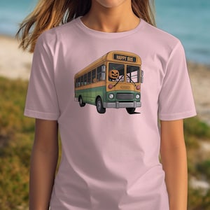 Puede incluir: Camiseta rosa claro con un diseño de autobús de dibujos animados. El autobús es amarillo y verde, con una cabeza de calabaza conduciendo. El texto "HAPPY BUS" está encima del parabrisas. El diseño está centrado en la camiseta.