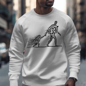 Puede incluir: Sudadera blanca con un gráfico negro que representa a una persona etiquetada como "PRESENTE" tirando de otra persona etiquetada como "PASADO". El diseño sugiere un tema de avanzar. La sudadera es de cuello redondo.