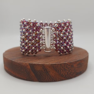May include: A beaded bracelet with a silver clasp. The beads are a mix of iridescent purple and silver.