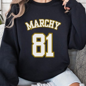 May include: Black sweatshirt with the word "MARCHY" in white and gold lettering above the number "81" in white with a gold outline. The sweatshirt is a crew neck style.