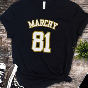 May include: Black t-shirt with a gold outline and the text "Marchy 81" in white.
