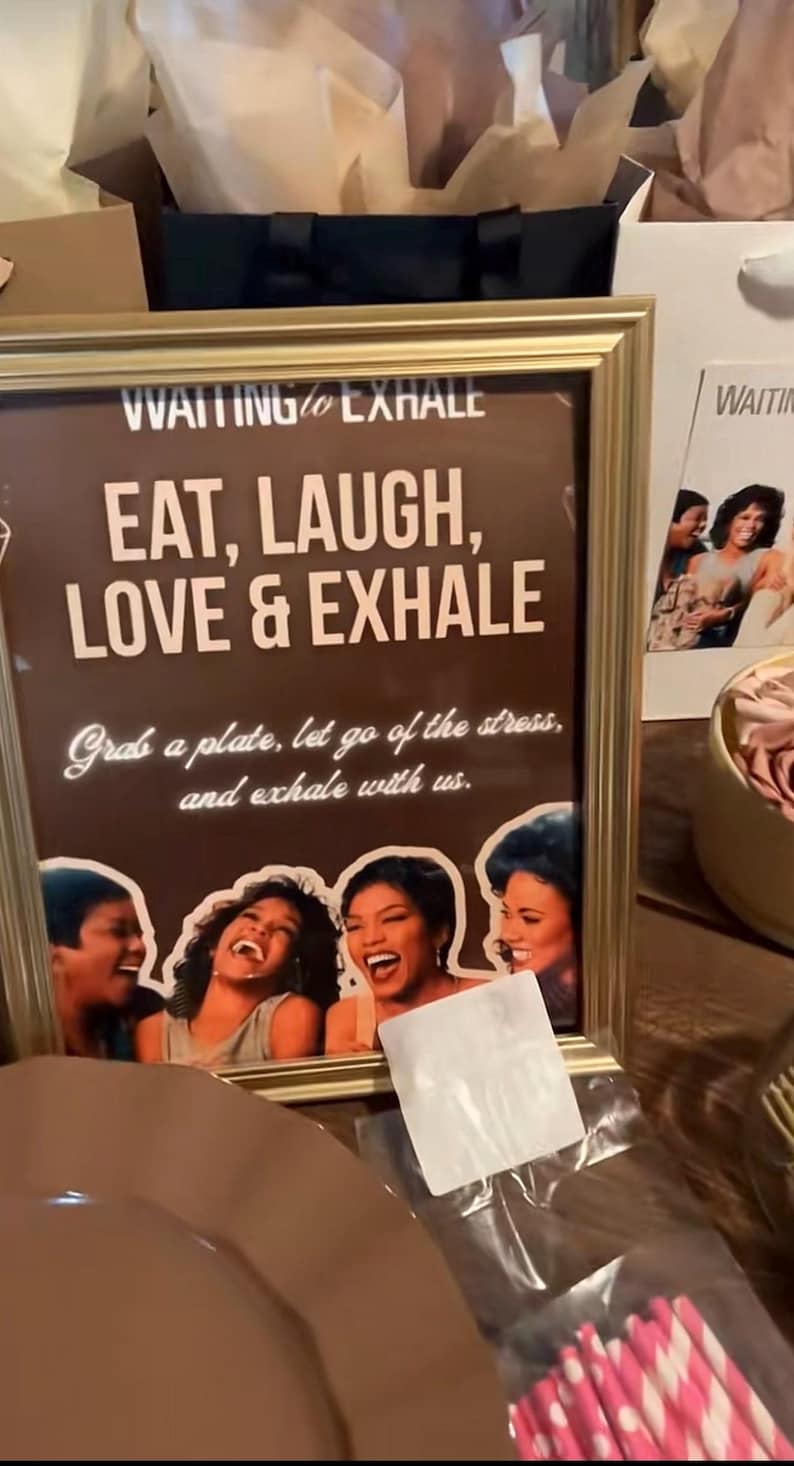 May include: A framed sign with the text "EAT, LAUGH, LOVE & EXHALE" in a brown background. The sign also includes the text "Grab a plate, let go of the stress, and exhale with us." and images of laughing women.
