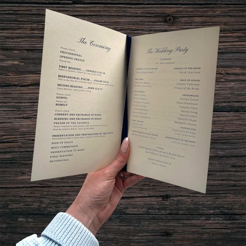 May include: A wedding program, open to display the ceremony details and wedding party names. The cream-coloured pages are bound with a dark blue spine. The program is held against a dark wood background, with text in a classic font.