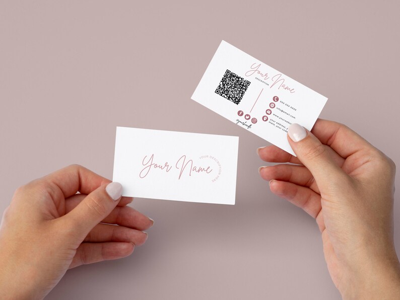 May include: Two white business cards with pink text. The top card has a QR code and social media icons. The text on the card reads "Your Name" and includes contact information. The bottom card has the text "Your Name" in cursive.