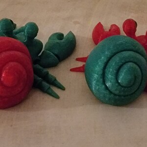 May include: Two 3D printed hermit crabs, one with a red shell and green legs, the other with a green shell and red legs.