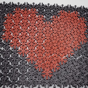 May include: A red heart shape made of small, interlocking, red snowflake-shaped tiles, surrounded by a larger square of black snowflake-shaped tiles.
