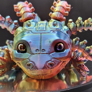 May include: A 3D printed iridescent axolotl figurine with a detailed, textured surface and large, expressive eyes. The figurine is painted in shades of blue, green, and gold.