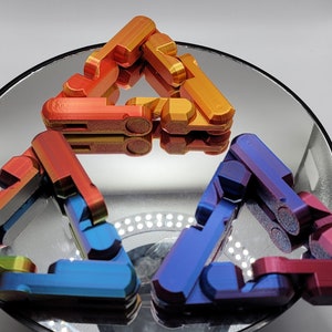 Può includere: Quattro giocattoli fidget in metallo a forma di triangoli, disposti in uno schema triangolare. I triangoli sono in tonalità di blu, verde, arancione e rosso.