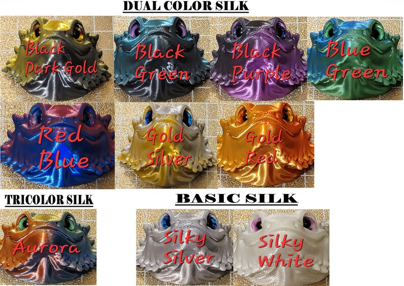 May include: A collection of 3D printed figurines with different color combinations. The figurines are of a bearded dragon with a textured surface. The colors include black, dark gold, green, purple, blue, red, gold, silver, and white. The text "Dual Color Silk", "Tricolor Silk", and "Basic Silk" is displayed above the figurines.