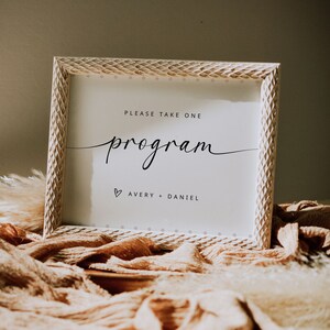 Puede incluir: Marco de madera blanco con un letrero que dice "Por favor, tome un programa" con los nombres Avery y Daniel debajo.