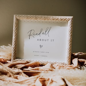 Op de afbeelding: Een wit ingelijst bord met de tekst "Read all about it" in zwarte cursieve letters. Onder de tekst staat een klein hartje, gevolgd door "please take one" en de namen "Avery - Daniel".