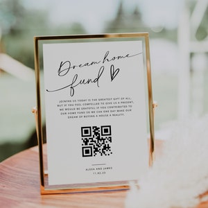May include: A gold-framed sign with a white background and black text that reads "Dream home fund ♥". The sign also includes a QR code and the text "Alexa and James 11.02.23".