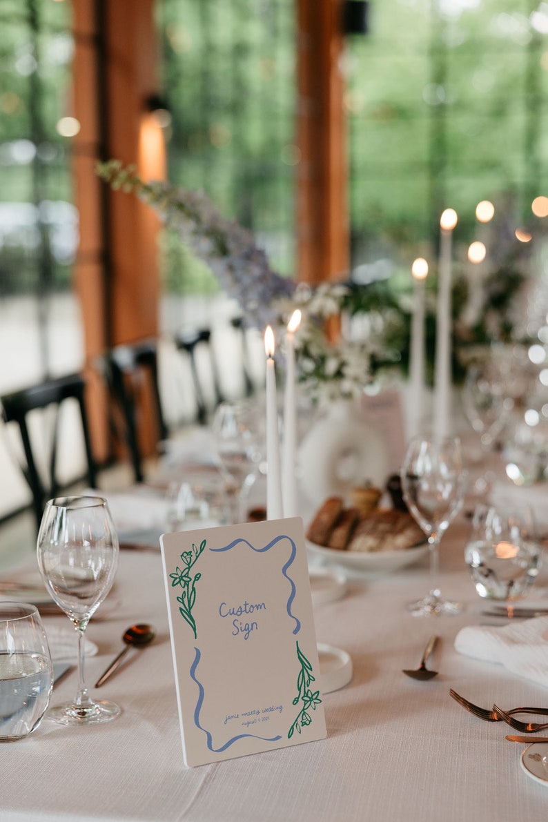 Op de afbeelding: Een wit bord met een blauwe en groene rand en bloemmotieven. Het bord heeft de tekst "Custom Sign" en "Jane & Walter Wedding August 1, 2021".