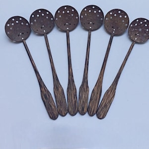 Puede incluir: Seis cucharas ranuradas de madera con cabezas redondas y mangos largos y delgados. Las cucharas son de color marrón oscuro con un patrón de vetas de madera natural. Las cabezas están perforadas con pequeños agujeros.