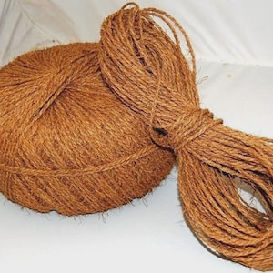 May include: A ball of brown twine and a bundle of the same twine. The twine is tightly wound into a ball shape and a separate bundle. The twine is a natural brown colour and appears to be made of a fibrous material.