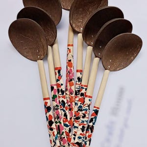 May include: A collection of wooden spoons with brown coconut shell bowls and patterned handles. The handles feature a colorful design with red, blue, pink, and black accents. The spoons are arranged in a fan shape.