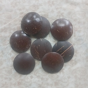 May include: Eight dark brown, circular objects with a polished surface and a natural, speckled appearance. Light-coloured streaks are visible on the objects. They are arranged on a patterned, off-white surface.