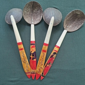 May include: Four handcrafted coconut shell spoons with wooden handles. The handles are painted with festive Christmas designs, including Santa Claus figures and the words "Merry Christmas." The spoons have a natural wood grain finish with red and white accents.