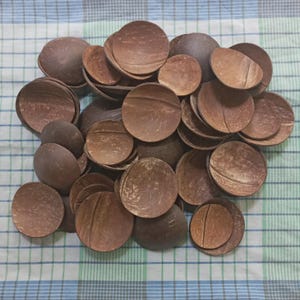 May include: A pile of brown coconut shell halves, varying in size and shape. The shells are arranged on a checkered fabric. The natural wood grain is visible on the shells. The shells are made of natural material.