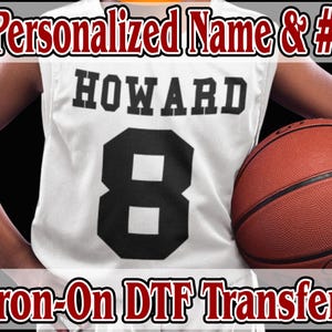 May include: White basketball jersey with the name "HOWARD" and the number "8" printed in black. The jersey is being held by a person wearing a basketball jersey. The text "Iron-On DTF Transfer" is printed in red at the bottom of the image.